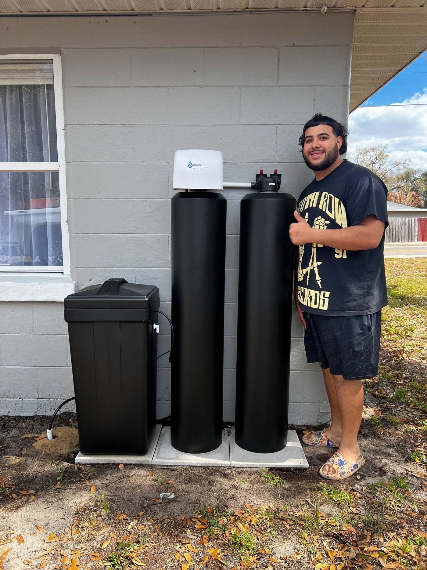 Homeowner beside a newly installed exterior water softener and brine tank